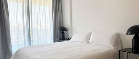 Un dormitorio con una cama grande, dos mesitas de noche y una ventana con cortinas.