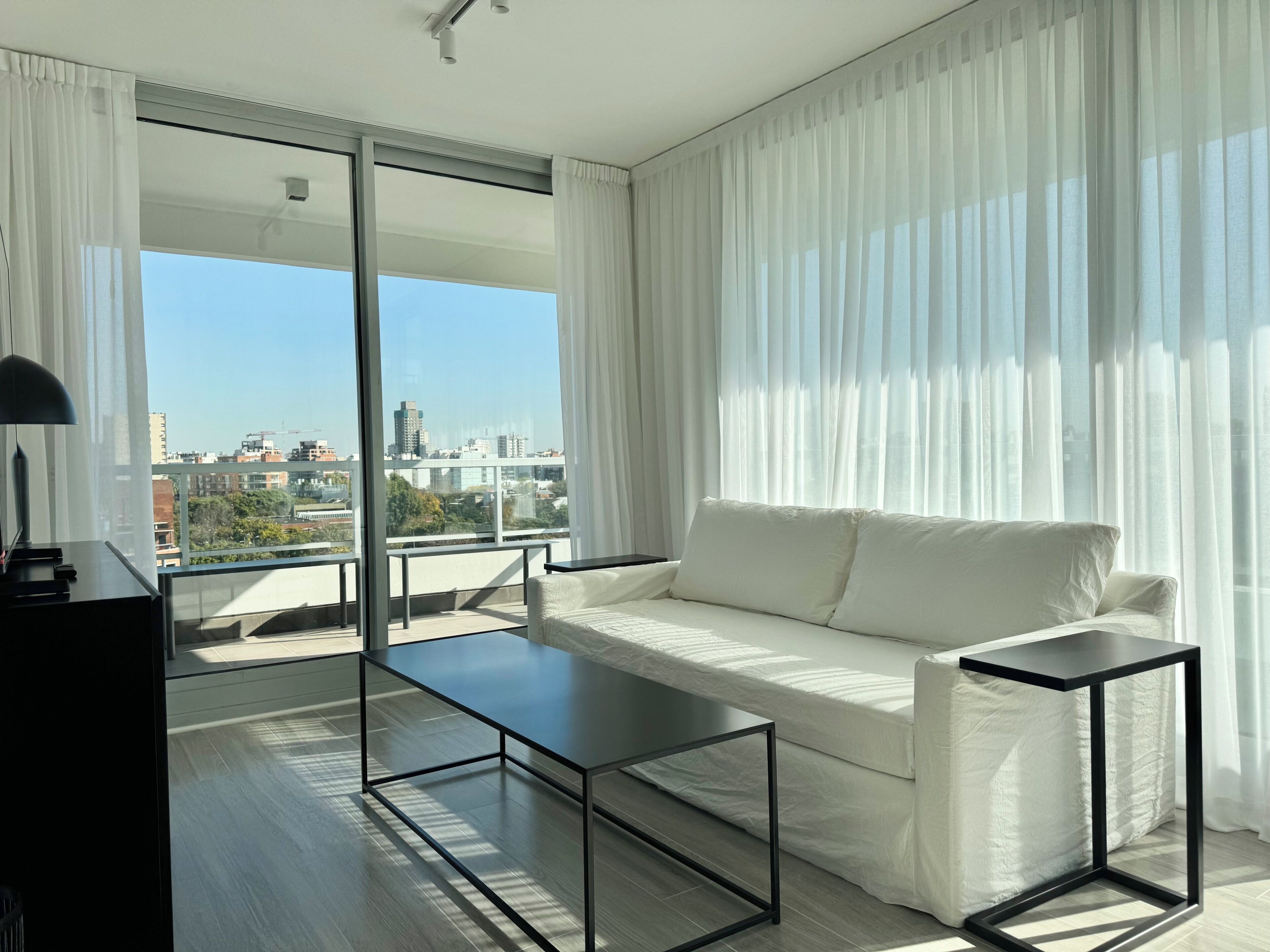 Ein modernes Wohnzimmer mit einem weißen Sofa, einem schwarzen Couchtisch und Blick auf die Stadt durch große Fenster.