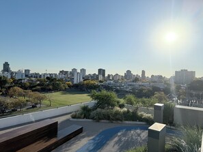 A rooftop terrace with a view of a city skyline, a grassy area, and a modern bench. - Luxurious and Bright 2-Bedroom, 2-Bathroom Home in Concepción Live (Buenos Aires)