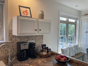 A kitchen with white cabinets, a coffee maker, a kettle, and a bowl of fruit on the counter.