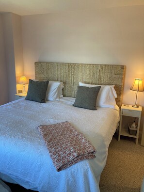 A neatly made bed with a patterned throw, two bedside lamps, and a nightstand with a bottle and basket.