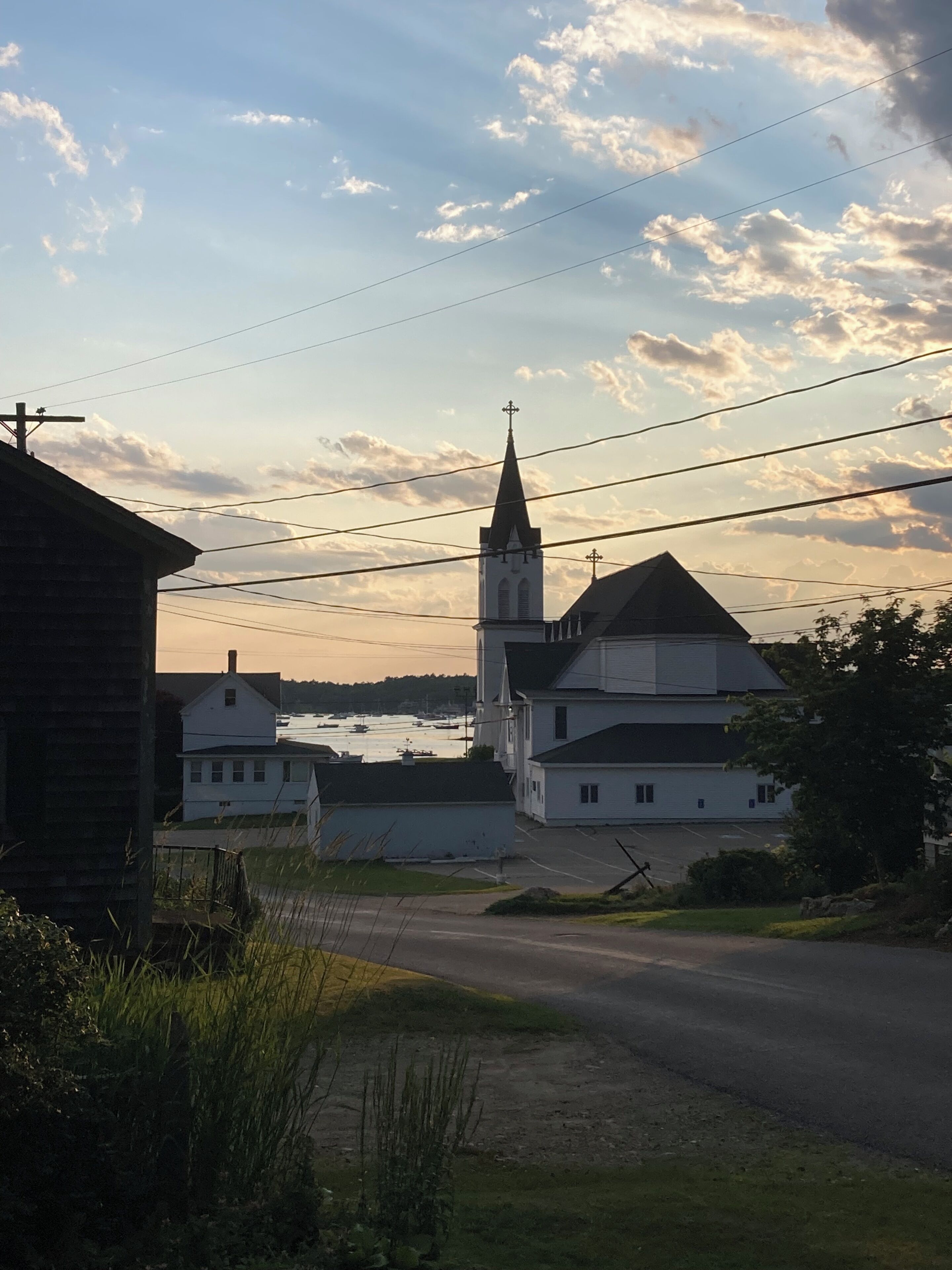 A church with a tall steeple, surrounded by residential buildings and a body of water in the background.