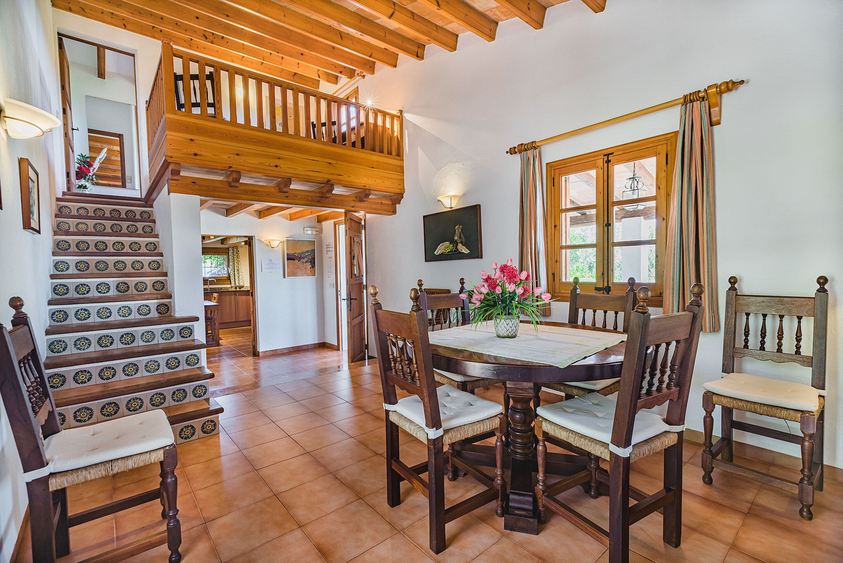 A dining area with a wooden table, chairs, and a staircase with patterned tiles.