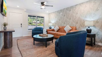 Un salon comprenant un canapé, deux fauteuils, une table basse, un ventilateur de plafond et une grande fenêtre.
