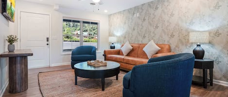 Una sala de estar con un sofá, dos sillones, una mesita de centro, un ventilador de techo y un amplio ventanal.