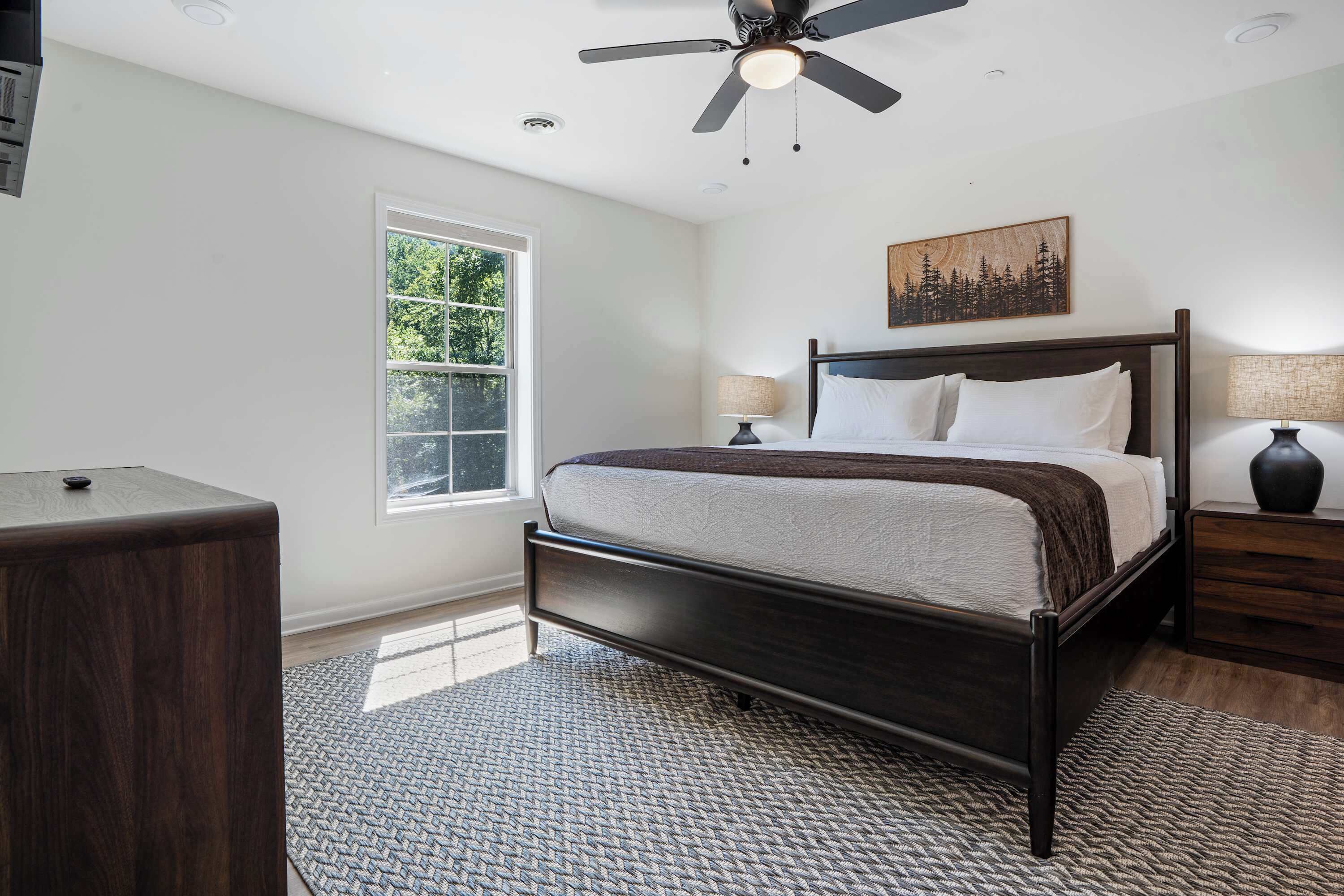 Une chambre à coucher avec un lit, un ventilateur de plafond, une fenêtre et une table de chevet.
