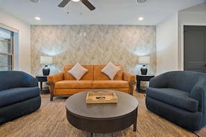 Ein Wohnzimmer mit einem braunen Sofa, zwei Sesseln, einem runden Couchtisch und einer Wand mit Muster.