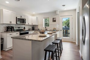 Cozinha moderna com armários brancos, uma ilha central com banquetas, micro-ondas embutido e máquina de café.