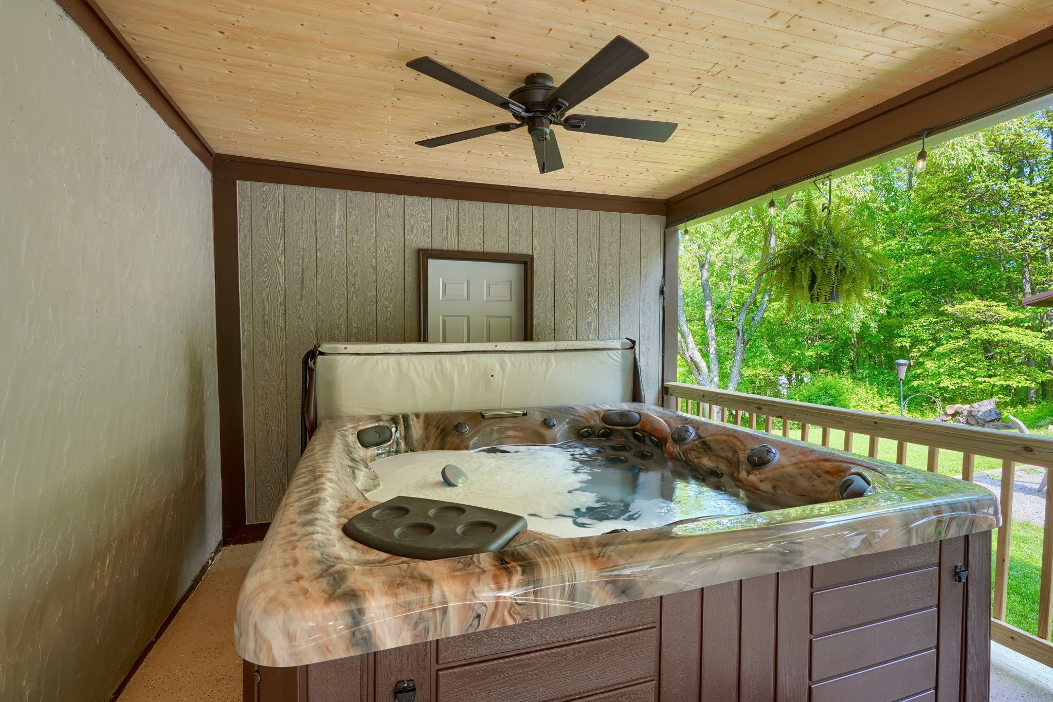 A hot tub with a wooden exterior, a ceiling fan, and a door in the background.