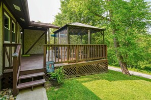 Eine Holzterrasse mit überdachter Sitzecke, ein Schild, das einen Sieger beim Versteckspiel ausweist, und einer üppigen, grünen Rasenfläche.