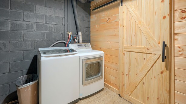 A laundry area with a washing machine and dryer, a wooden door, and a concrete wall. - Hideaway Pines Cabin (Logan)