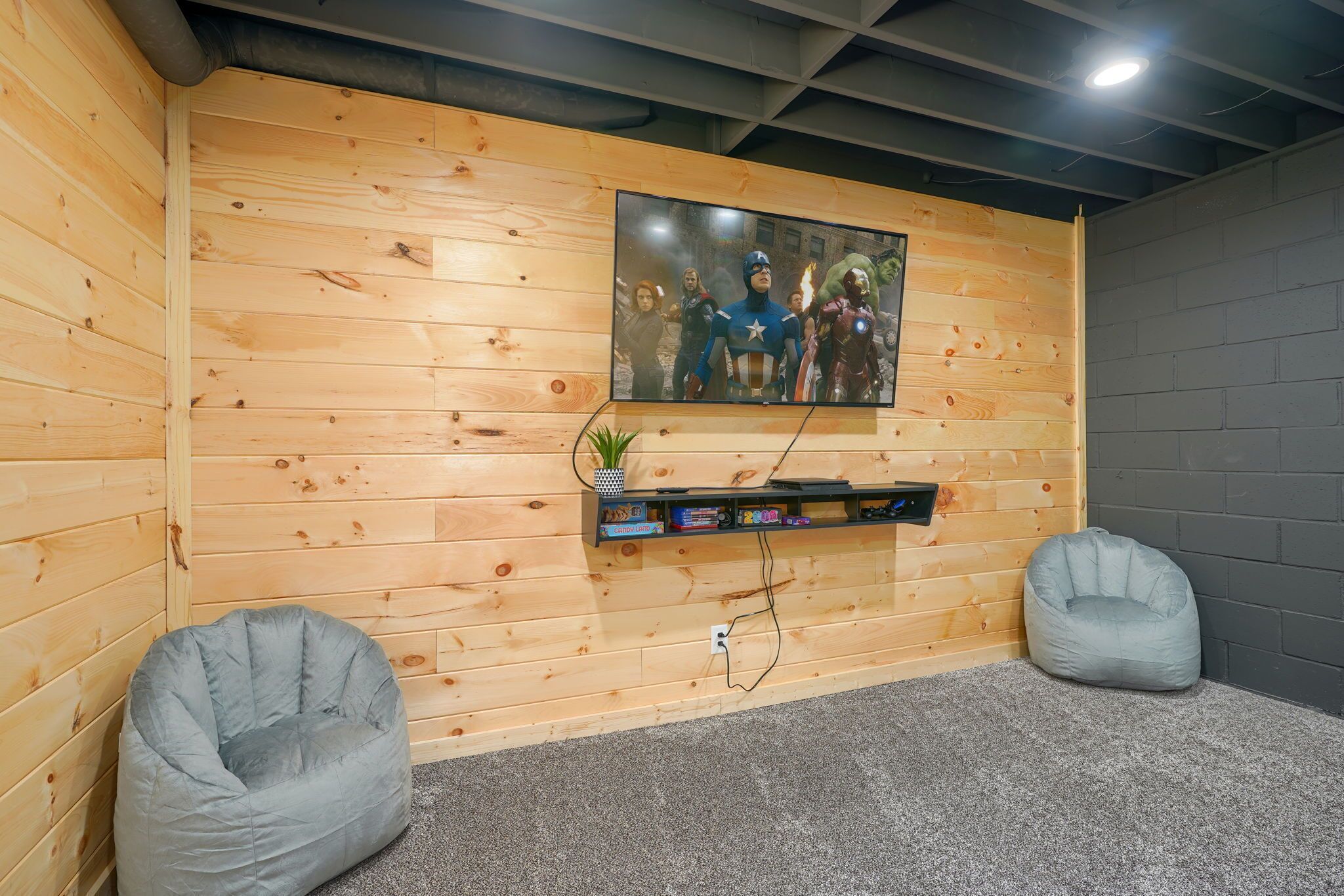 A room with wooden panel walls, a mounted TV, a shelf with books, and two bean bag chairs.