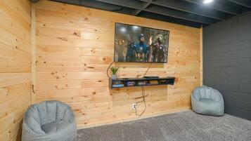 A room with wooden panel walls, a mounted TV, a shelf with books, and two bean bag chairs.