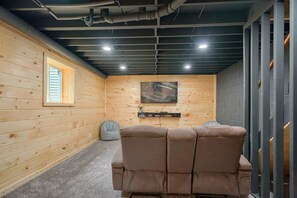 Ein Zimmer mit Holzwand, einer Decke mit freiliegenden Rohren, einem angebrachten Fernseher und einem braunen Ledersofa.