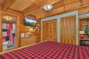 Ein Interieur einer Holzhütte mit einem Bett, einem Fernseher, einem Holzschrank und einem Badezimmer mit Duschvorhang.