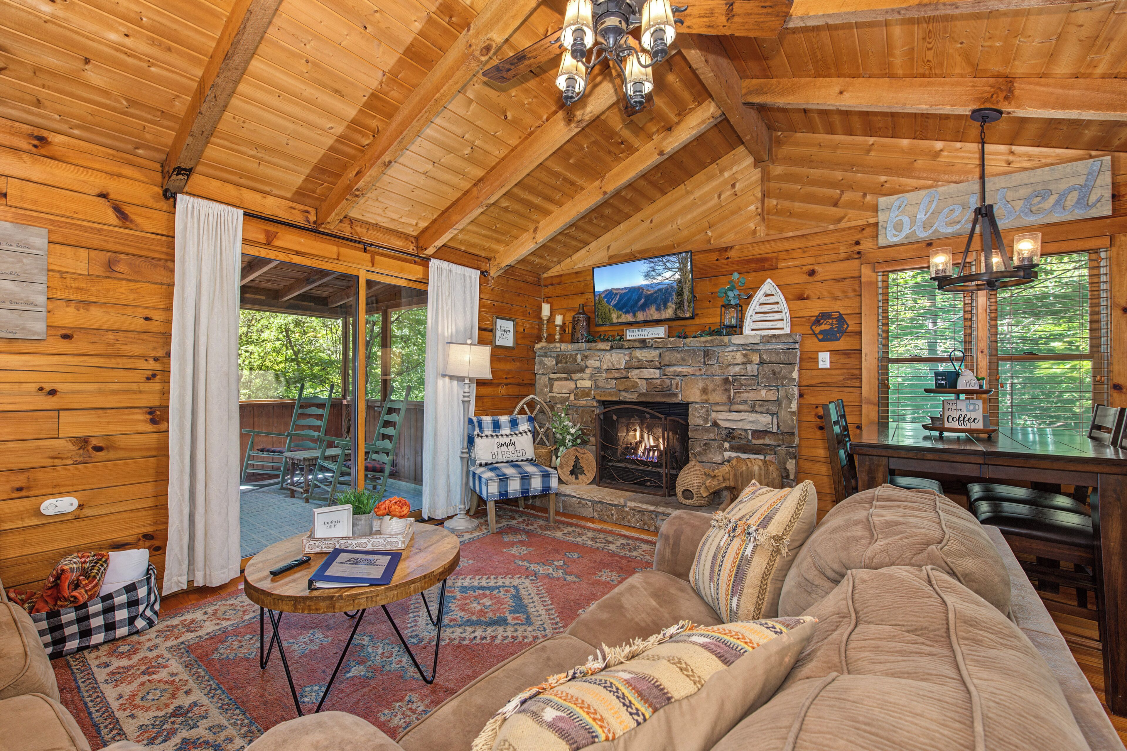 A cozy log cabin interior with a stone fireplace, wooden furniture, and a television mounted on the wall.