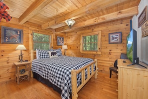 Een houten chalet van binnen met een bed, twee bedlampen, een televisie en ingelijste foto's aan de wanden.
