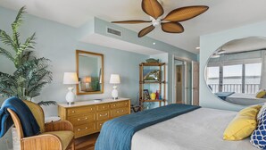 Quarto com cama, cadeira, cômoda, espelho e ventilador de teto.