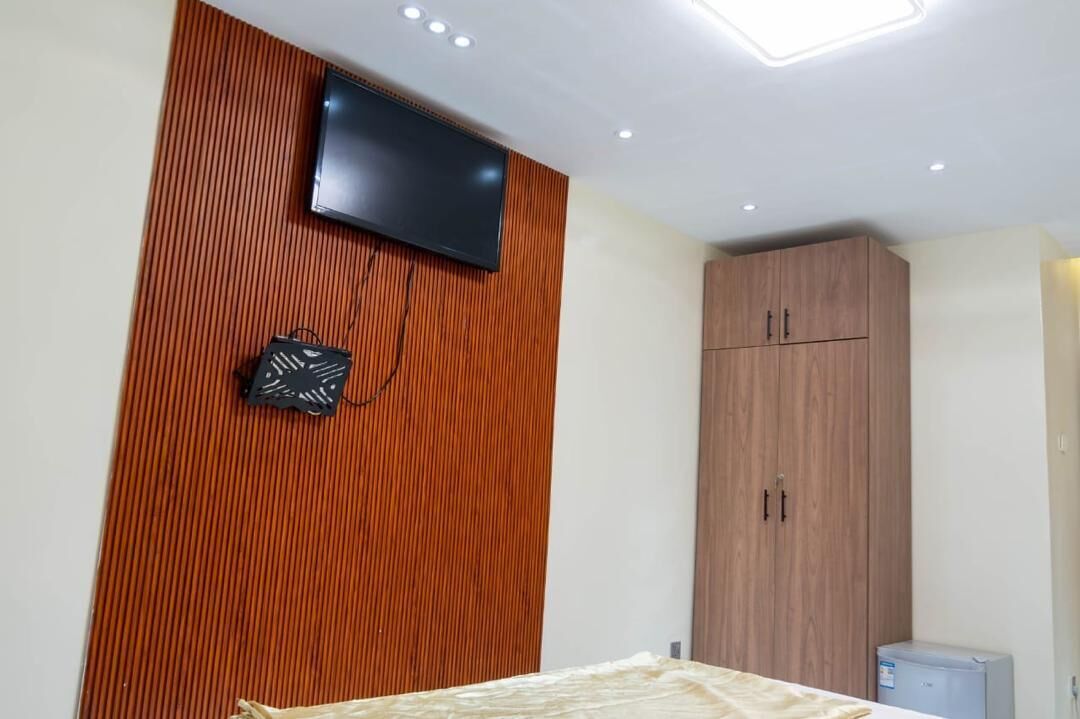 Une chambre avec un mur recouvert de panneaux de bois, un téléviseur à écran plat fixé au-dessus, et une armoire à deux portes.