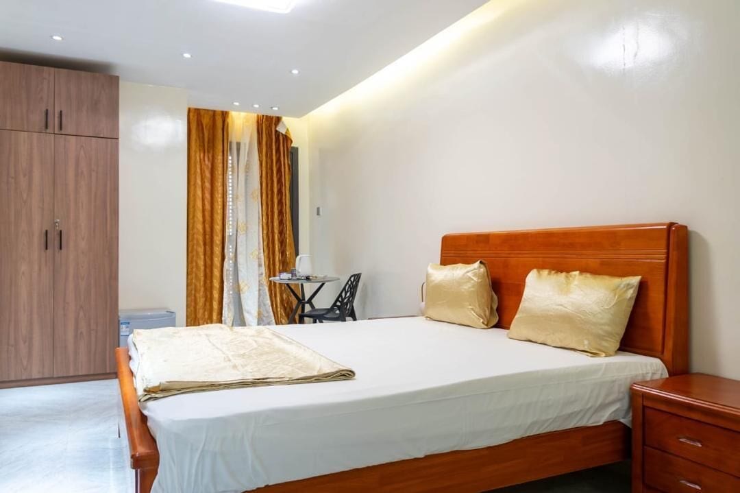 Une chambre à coucher avec un lit en bois, une table de chevet, une petite table avec une chaise et une armoire.