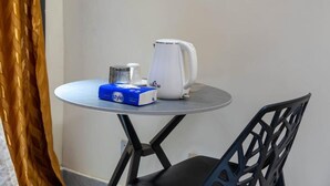 Een klein rond tafeltje met een witte waterkoker, een blauwe doos met de tekst 'style' en een metalen bak.