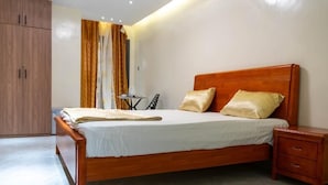 Een slaapkamer met een houten bed, een nachtkastje, een garderobe en een kleine tafel met een stoel.