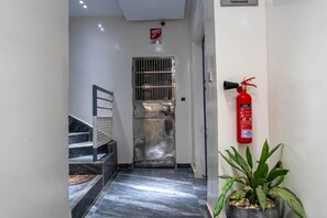Un pasillo con una reja metálica, un extintor y una planta en maceta.