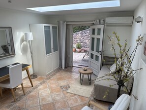 Ein Zimmer mit Dachfenster, Schreibtisch, Stuhl, einer Couch, einem kleinen Tisch und einer Topfpflanze.
