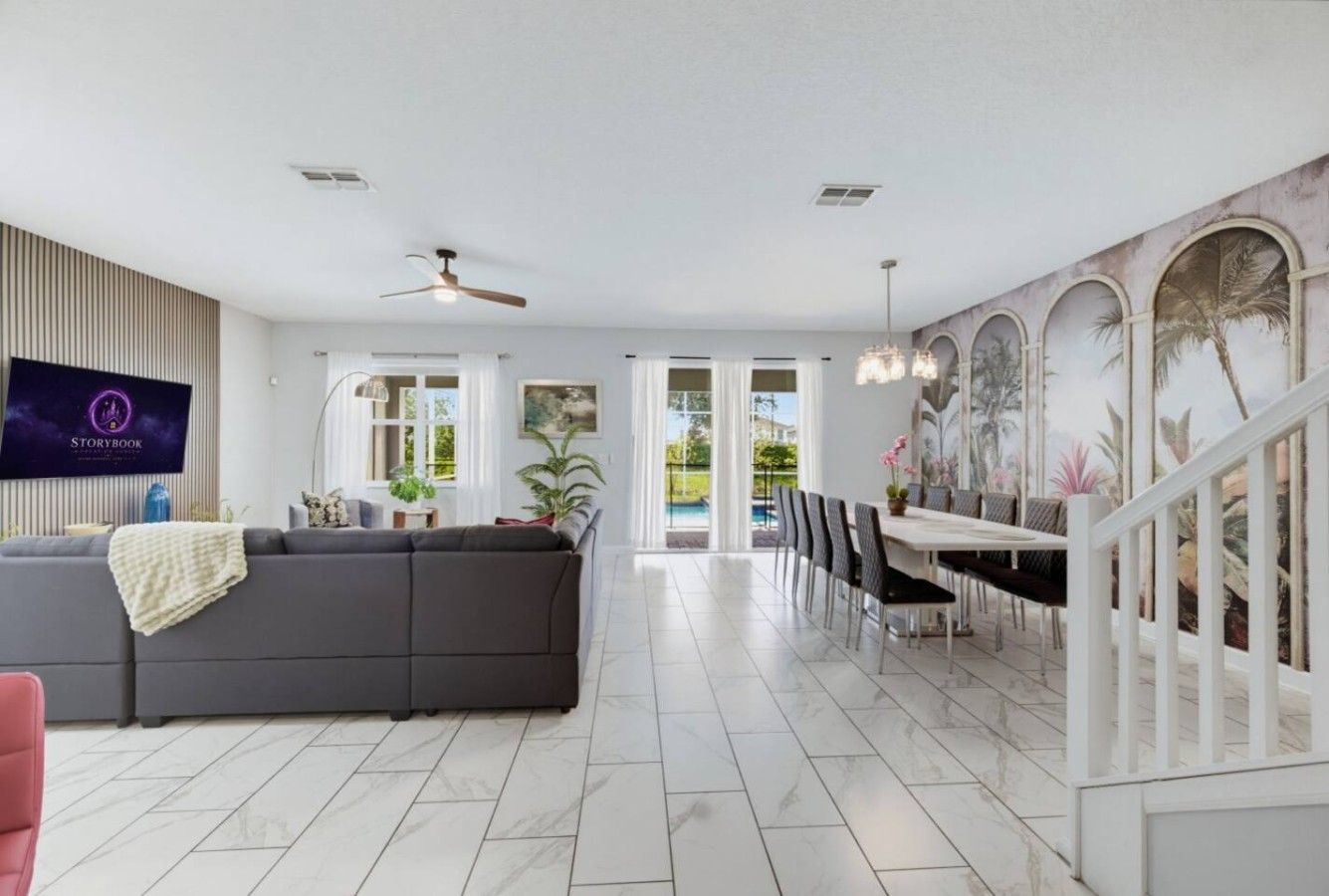 A spacious living area with a grey sofa, a flat-screen TV, and a dining area with chairs and a table.