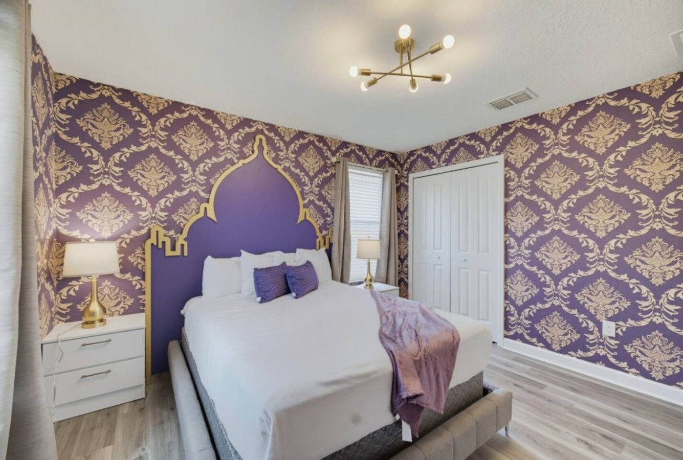 A bedroom with a bed, nightstand, lamp, and a decorative ceiling light fixture.