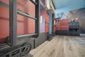 A train-themed room with a wooden floor, a red train carriage, and a black train engine. - Private Pool, Theater & Themed Rooms (Four Corners)