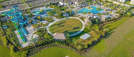 An aerial view of a resort with a swimming pool, water slides, and a tennis court.