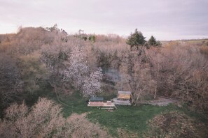 Ländliche Landschaft mit einem kleinen Haus, umgeben von Bäumen und blauem Himmel.
