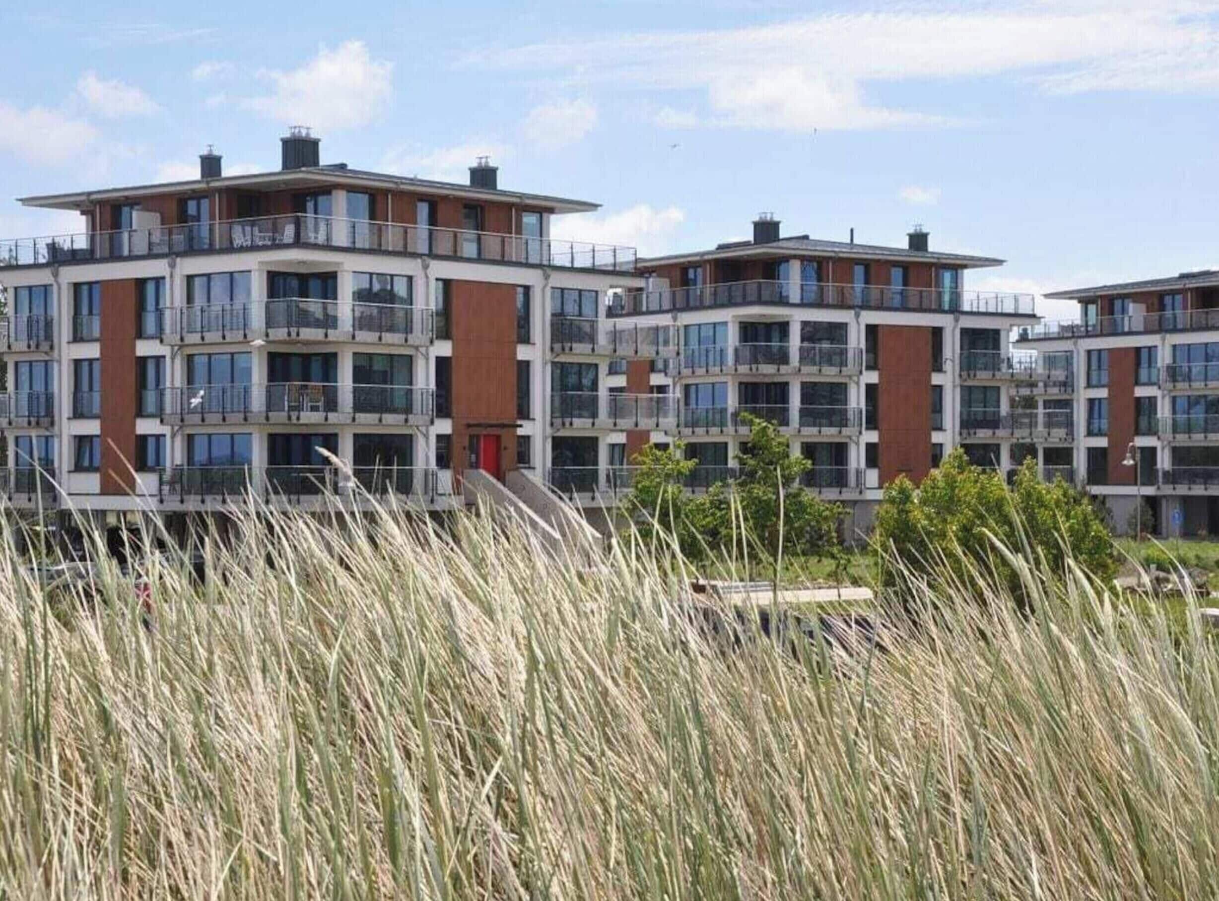 Un moderno edificio residencial de varios pisos con balcones y grandes ventanales.
