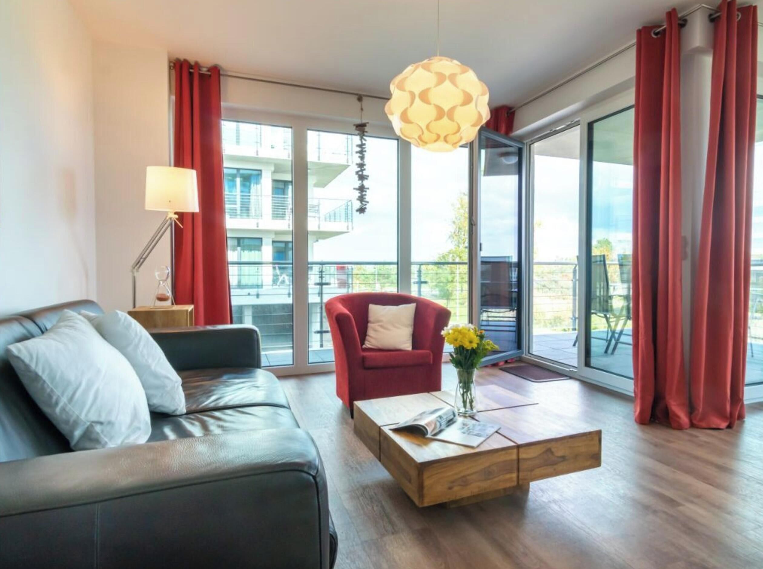 A modern living room with a leather sofa, a red armchair, a wooden coffee table with a vase of flowers, and a hanging light fixture.