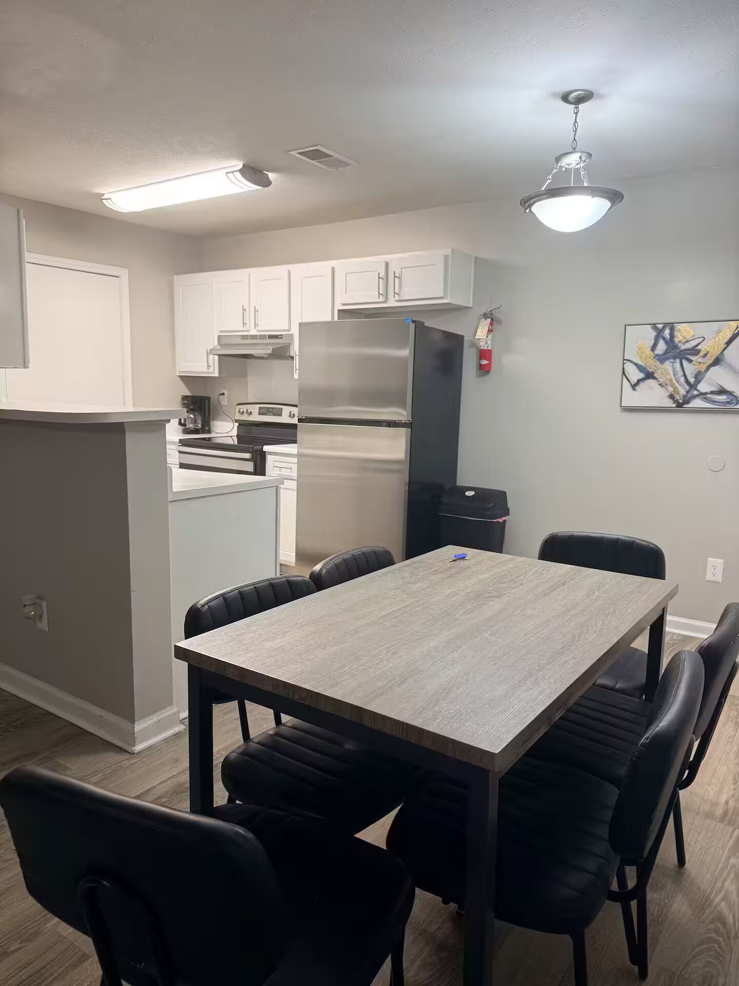 A modern kitchen with white cabinets, a stainless steel refrigerator, and a dining area with a wooden table and black chairs.