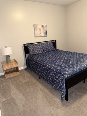 Ein Schlafzimmer mit einem Bett, einem Nachttisch, einer Lampe und einem Gemälde an der Wand.