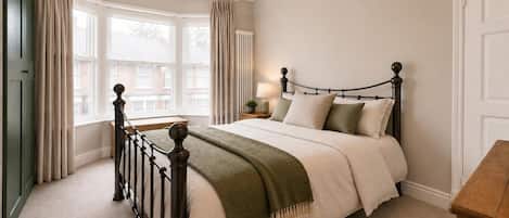 A bedroom with a bed, a nightstand, a lamp, and a window with curtains.