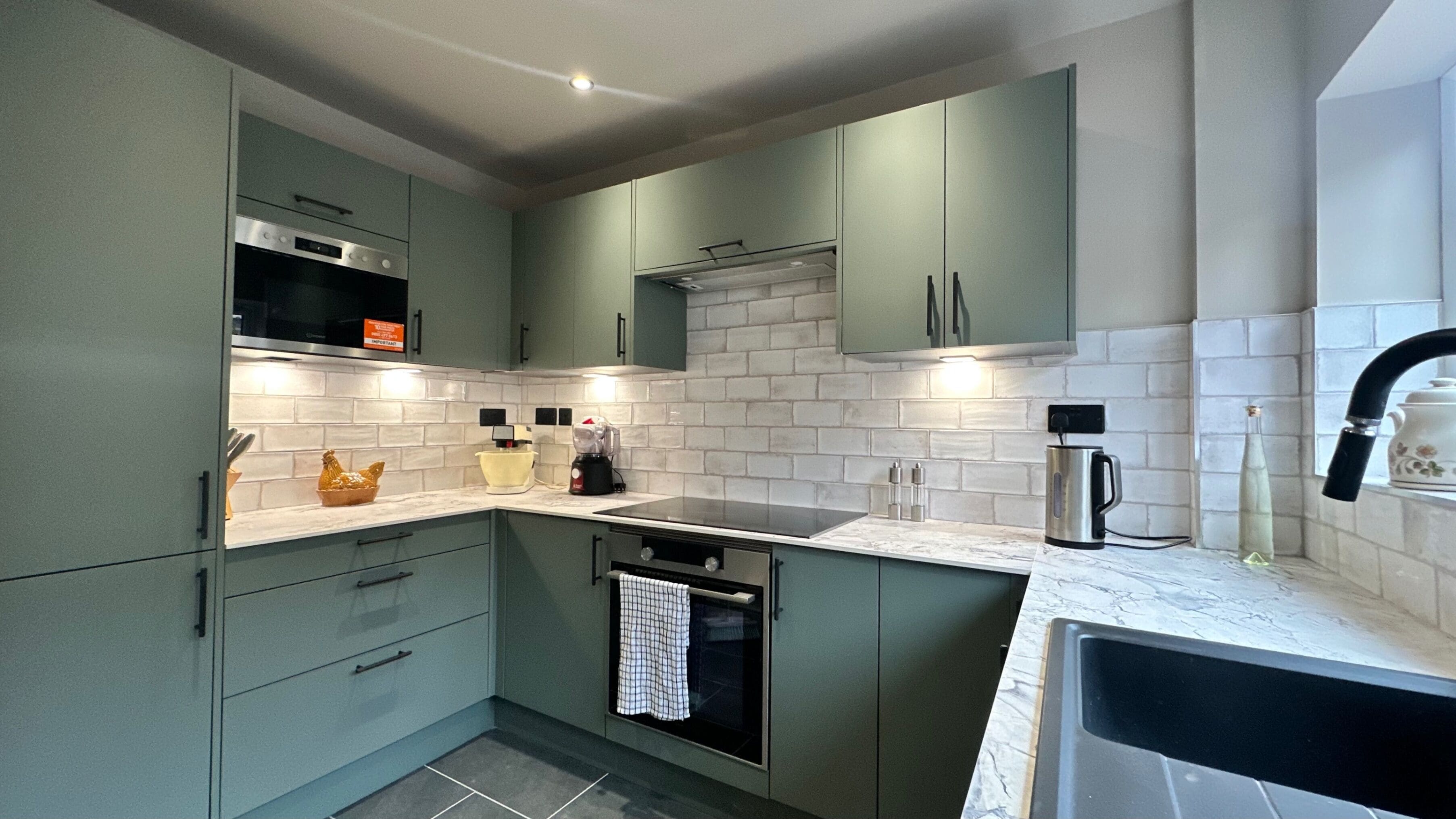 Una cocina moderna con armarios verdes, horno de acero inoxidable y salpicadero con azulejos blancos.