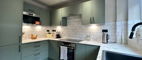 Una cocina moderna con armarios verdes, horno de acero inoxidable y salpicadero con azulejos blancos.