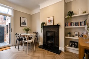 A cozy living room with a fireplace, a dining area with chairs, a bookshelf, and a framed picture of The Beatles. - Smart 3 Bed House, Minutes From Penny Lane (Liverpool)
