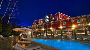 Una piscina amb gandules i ombrel·les, envoltada d'un edifici de diverses plantes i llums lluminoses.