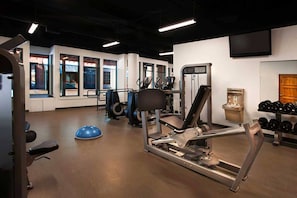 Un gimnasio con equipamiento de ejercicio, un televisor en la pared y una ventana con vistas al exterior.
