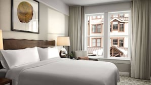 Una habitació d'hotel amb un llit gran, dues taules de nit, una finestra amb cortines i una obra d'art emmarcada a la paret.