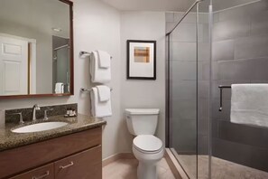 Et stilfuldt badeværelse med vaskebord i granit, toilet, et indrammet billede på væggen og en brusekabine i glas.