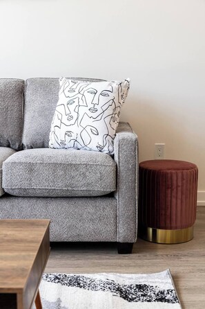 A grey sofa with a patterned pillow, a round ottoman with a gold base, and a wooden side table. - Luxury 3BR Penthouse • Central Location + City Views + Parking (Toronto)
