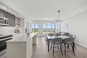 A modern kitchen with a central island, dining area with chairs, and large windows. - Luxury 3BR Penthouse • Central Location + City Views + Parking (Toronto)