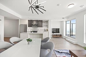 A modern kitchen with a central island, a dining area with chairs, and a large window providing natural light. - Luxury 3BR Penthouse • Central Location + City Views + Parking (Toronto)