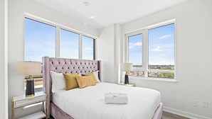 Ein Schlafzimmer mit einem großen Bett, zwei Nachttischen und Blick auf die Stadt durch große Fenster.