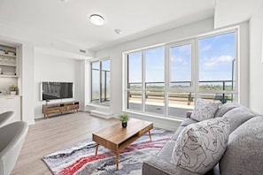A modern living room with a large window, a flat-screen TV, a wooden coffee table, and a grey sofa. - Luxury 3BR Penthouse • Central Location + City Views + Parking (Toronto)